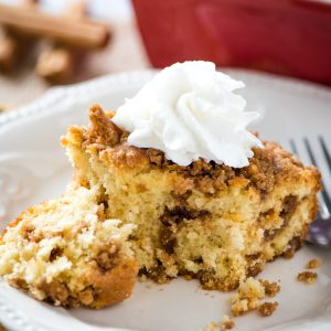 slice of cinnamon streusel coffee cake topped with whipped cream on white plate with fork