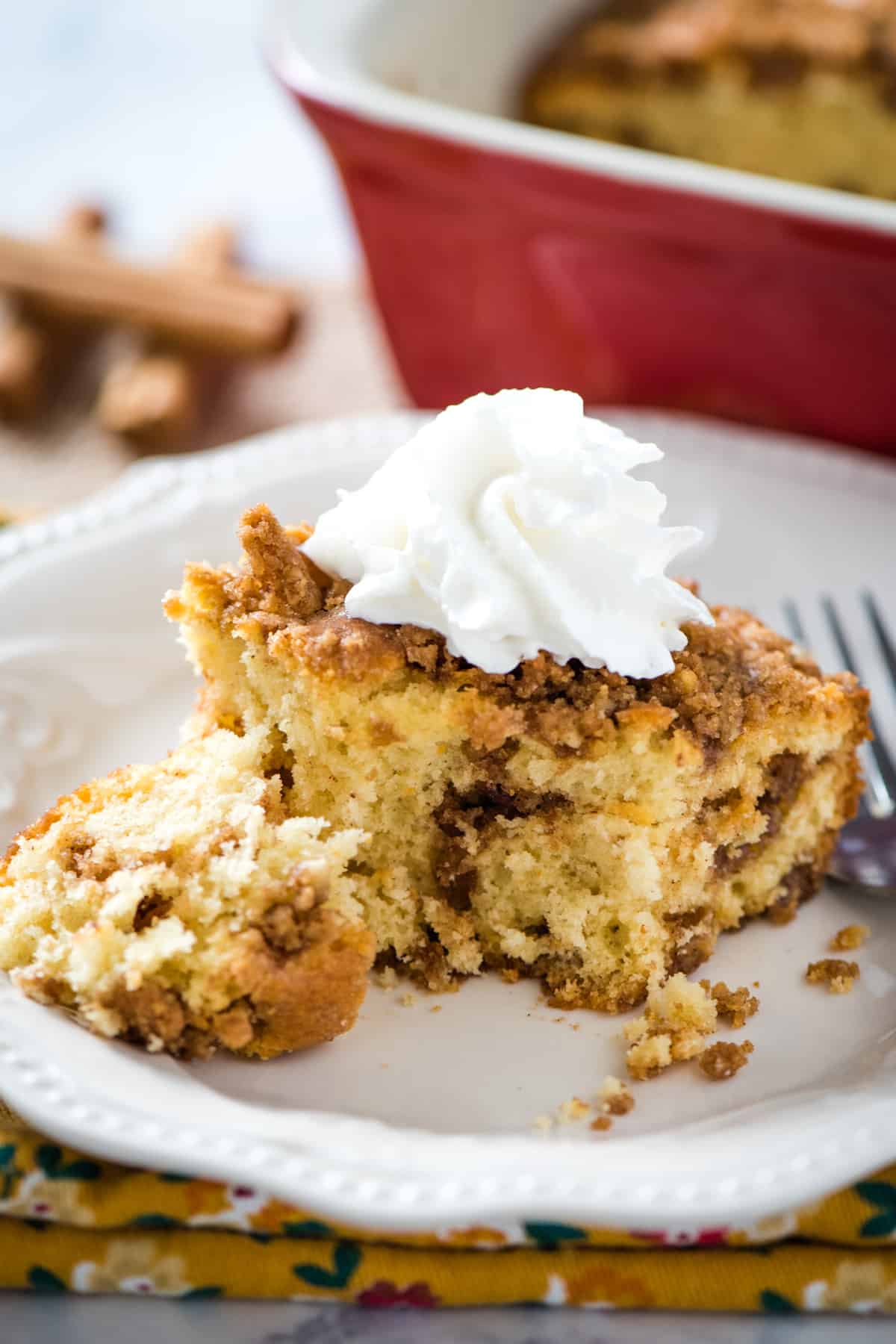 slice of cinnamon streusel coffee cake topped with whipped cream on white plate with fork
