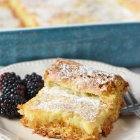 slice of gooey butter cake with blackberries on an ivory plate with fork