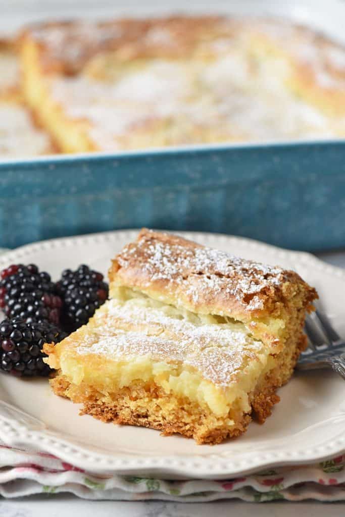 slice of gooey butter cake with blackberries on an ivory plate with fork