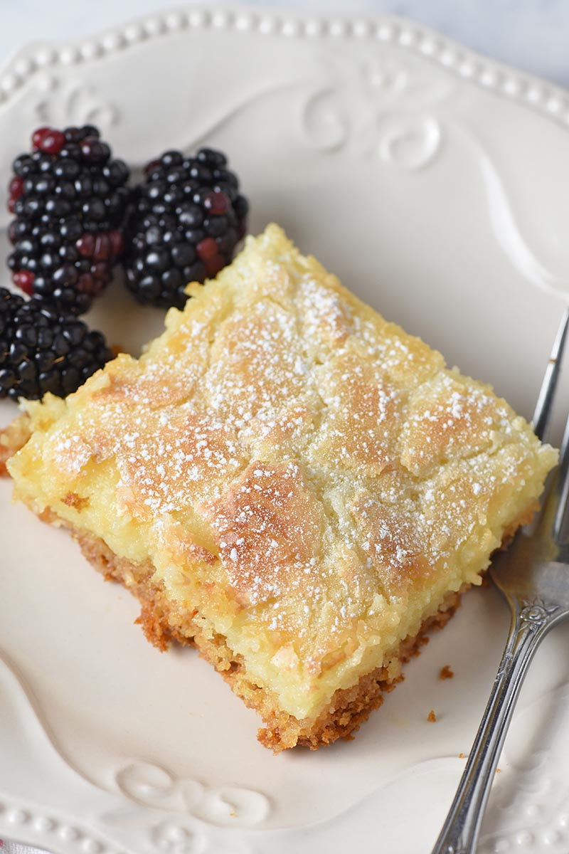 slice of gooey butter cake on ivory plate with blackberries