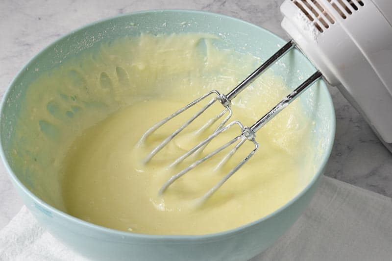 mixing ooey gooey butter cake filling in blue bowl with hand mixer