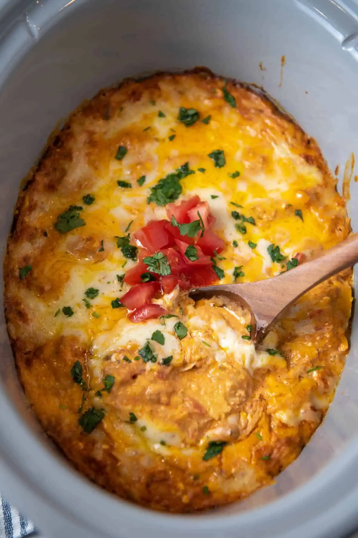 CrockPot chicken enchilada casserole with fresh tomatoes and cilantro in gray slow cooker with wooden spoon