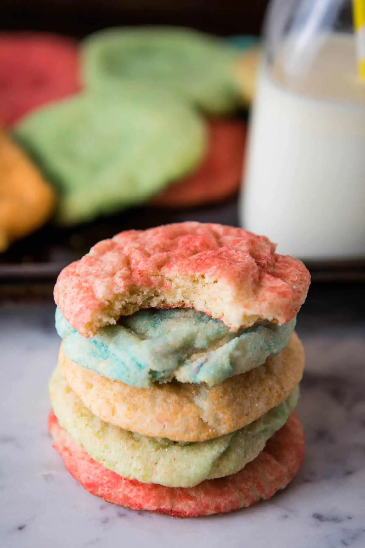 stack of Jello sugar cookies with glass of milk on white marble countertop