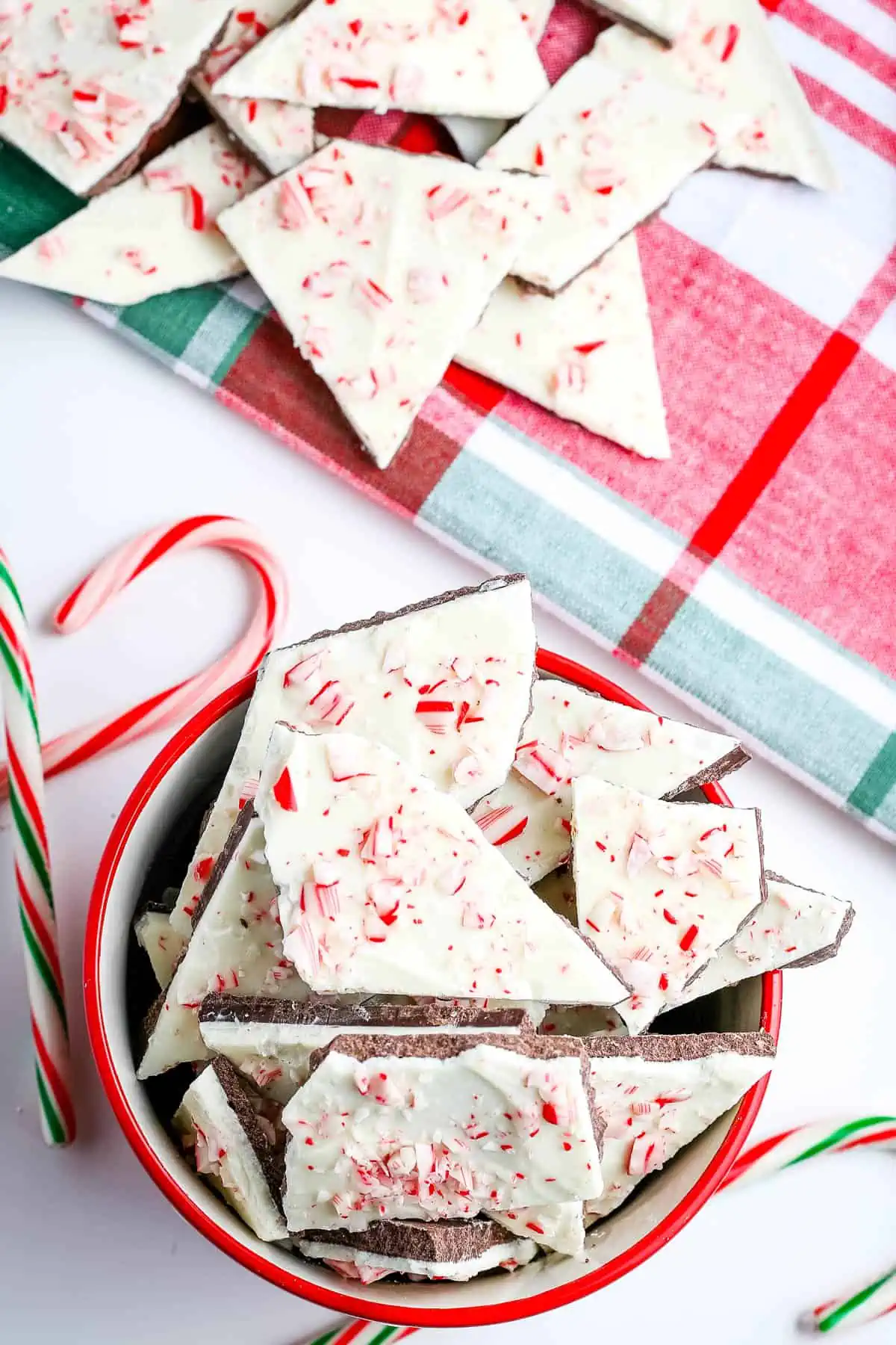 candy cane bark in red bowl and on Christmas plaid towel on white countertop with candy canes