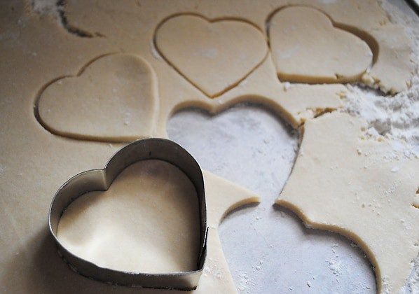 heart cookie cutter cutting heart shaped cookies from dough on floured surface