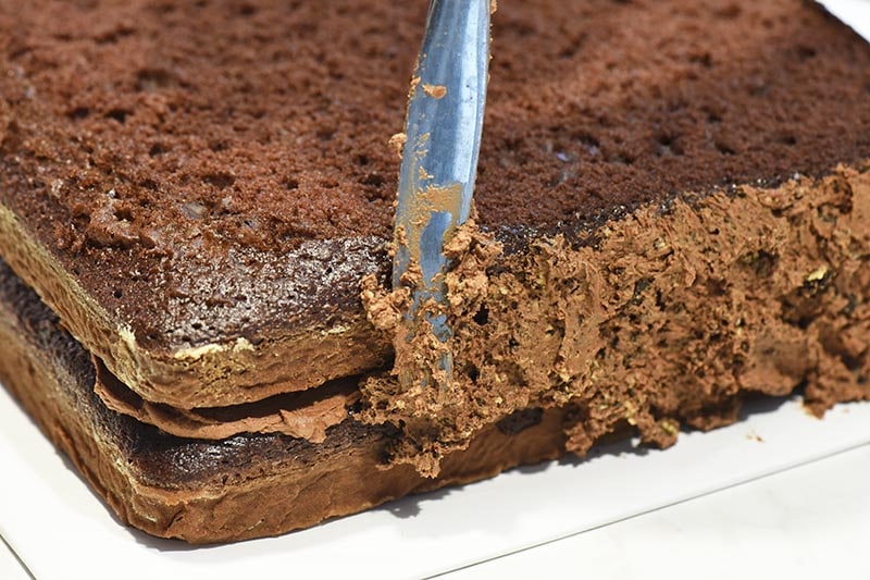 spreading chocolate buttercream dirt frosting on chocolate Minecraft cake with table knife