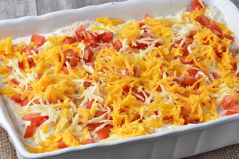 add shredded cheese to top of creamy chicken enchiladas in white baking dish