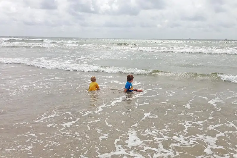 boys playing in the waves on San Jose Island beach, watching the ships go by out in the ocean