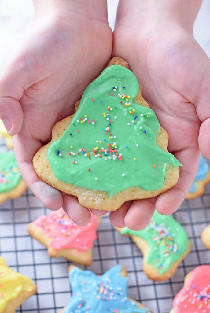 holding up a crisp cutout sugar cookie with green icing and multi-colored sprinkles closeup to the camera