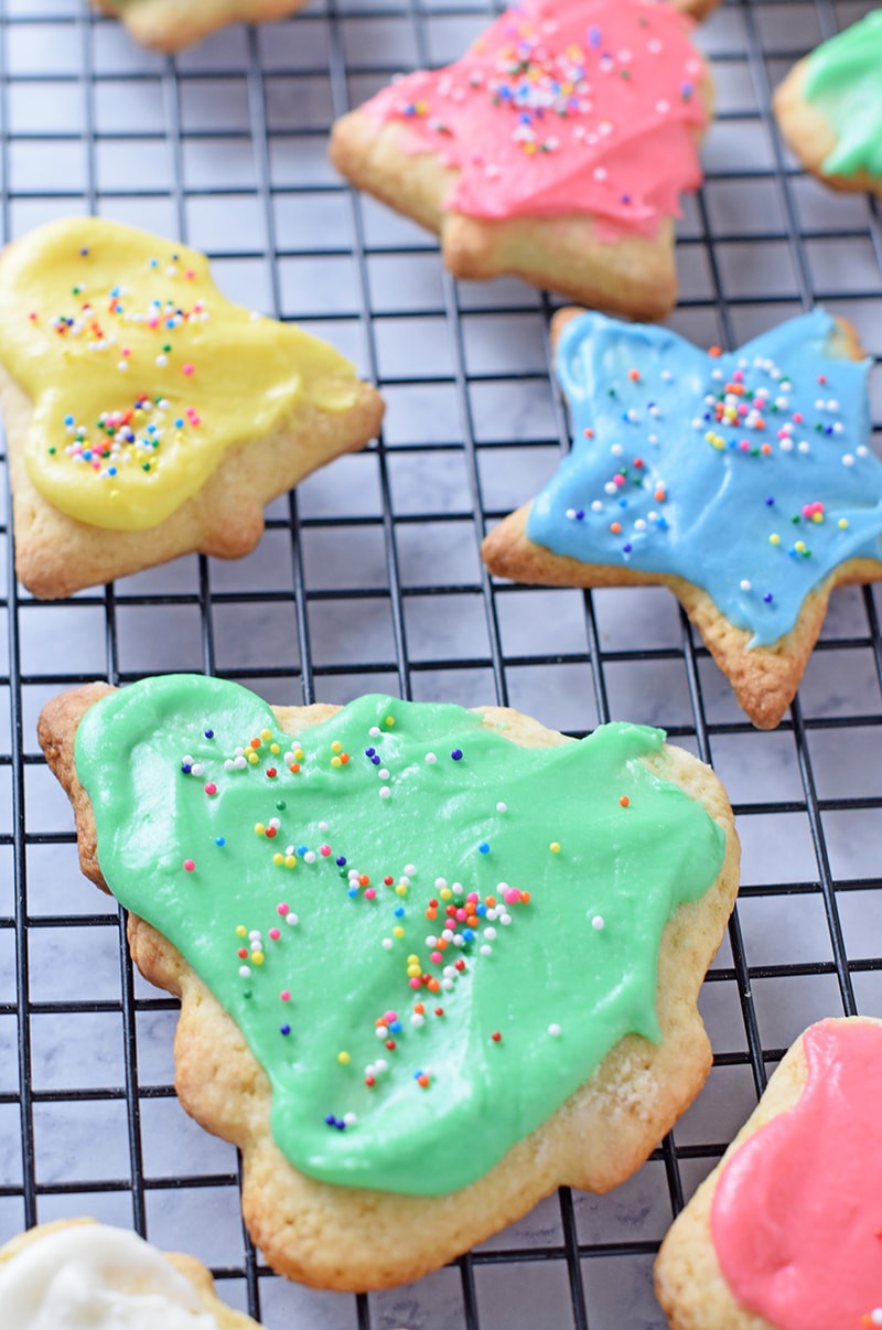 soft cut out sugar cookies decorated with colored icing and rainbow nonpareils sprinkles, sitting on black wire rack