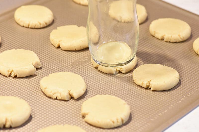 pressing dough into thumbprint Christmas cookies on OXO cookie sheet