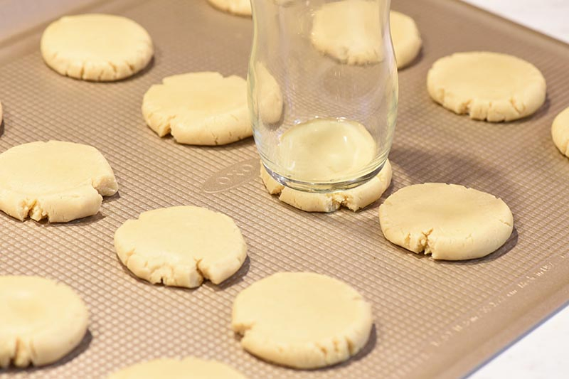 pressing dough into thumbprint Christmas cookies on OXO cookie sheet