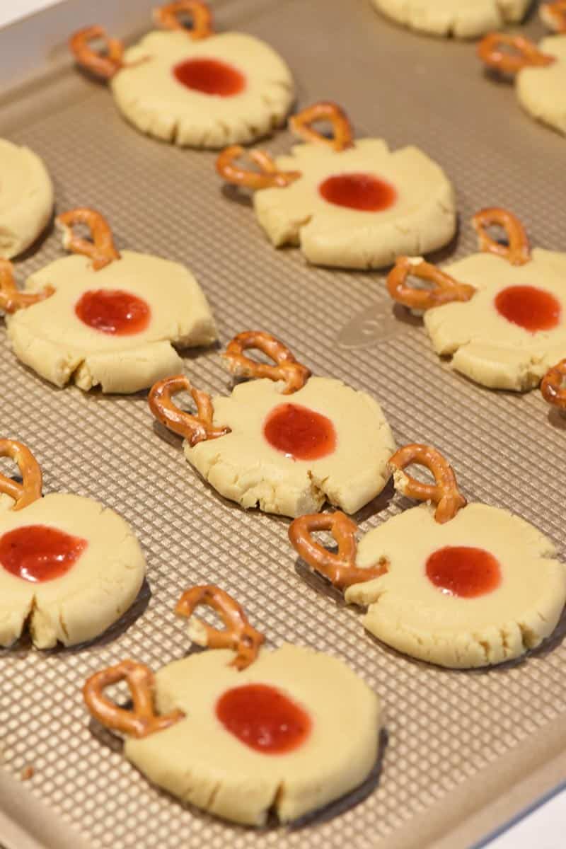 using mini twist pretzels as antlers for reindeer thumbprint cookies on cookie sheet