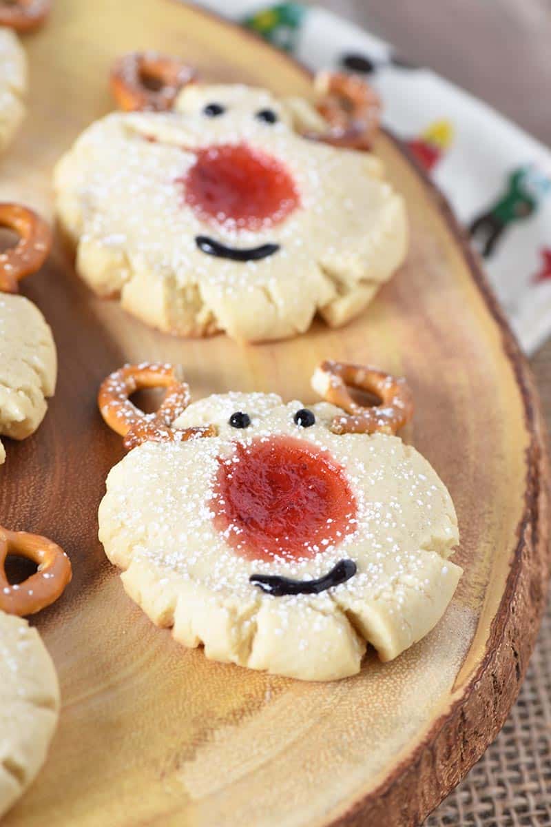 sprinkle powdered sugar on reindeer thumbprint Christmas cookies, thumbprint cookies on log platter