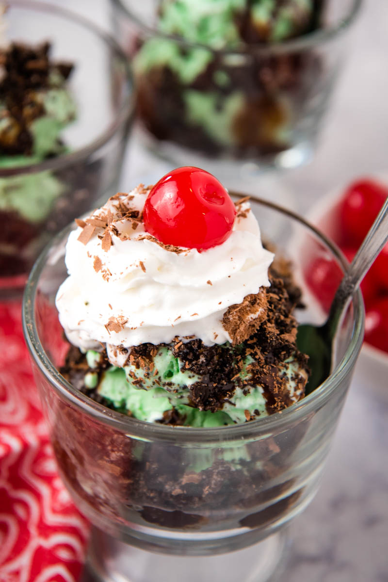 grasshopper sundae with mint chocolate chip ice cream, crushed Oreos, shaved chocolate, whipped cream, chocolate syrup, and maraschino cherry in sundae bowl with spoon