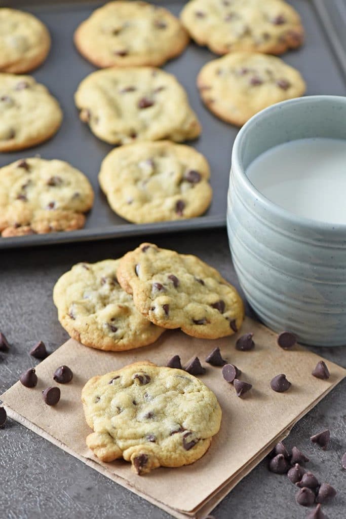 homemade soft chocolate chip cookies on brown paper bag and cookie sheet, served with blue mug of cold milk