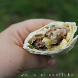 hand holding sausage and egg breakfast burrito