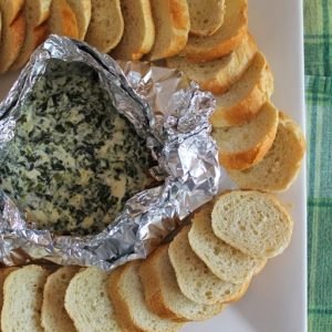 campfire spinach dip in aluminum foil bowl with slices of French bread