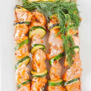 grilled salmon kabobs with zucchini and sliced lemon on white platter
