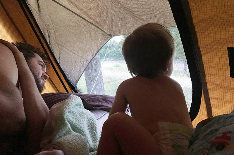 toddler looking out the window of rooftop tent while dispersed camping on a lake in Kansas