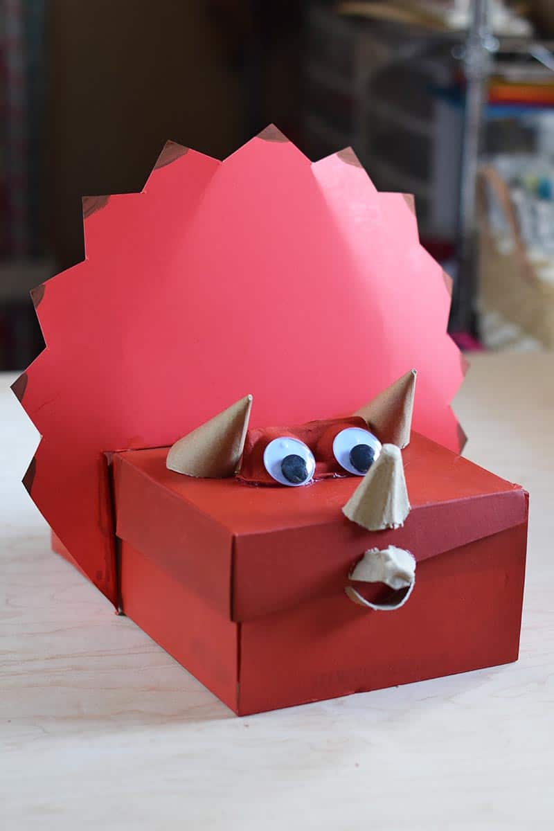 Triceratops dinosaur Valentine box painted red with eyes and horns, sitting on a wooden table
