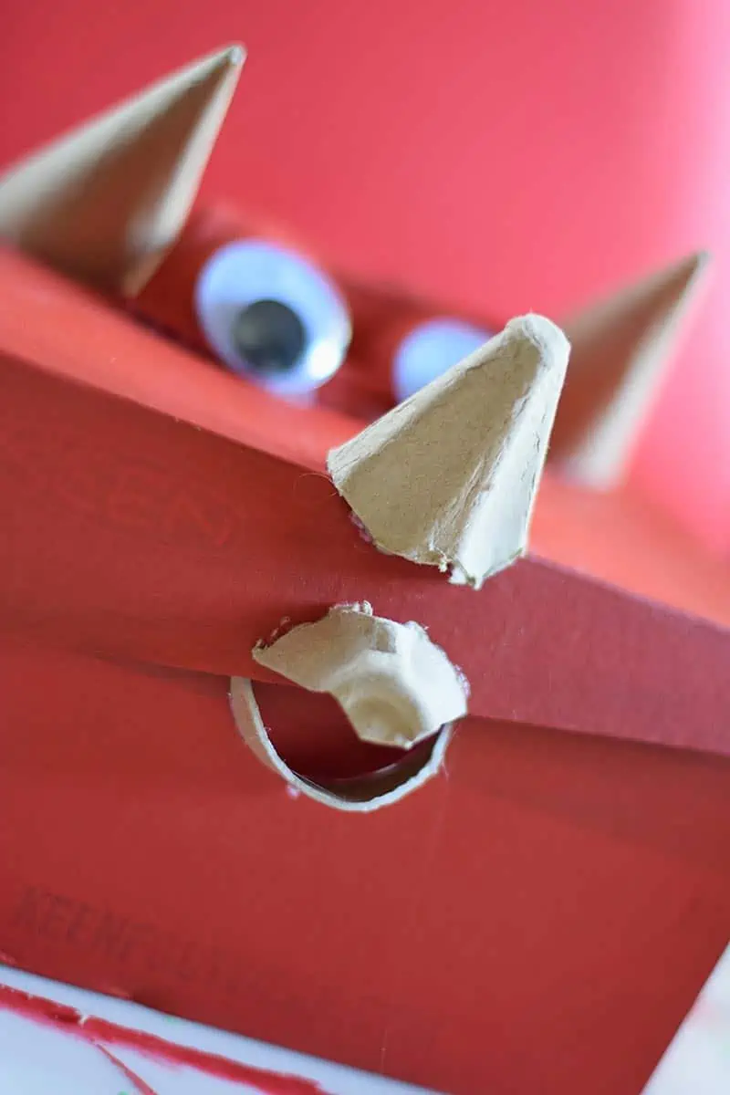 putting a Triceratops beak in place with pieces of an egg carton on a red Valentine box