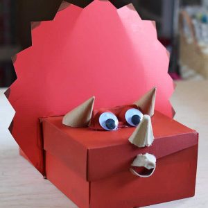 Triceratops homemade dinosaur Valentine box painted red with eyes and horns, sitting on a table