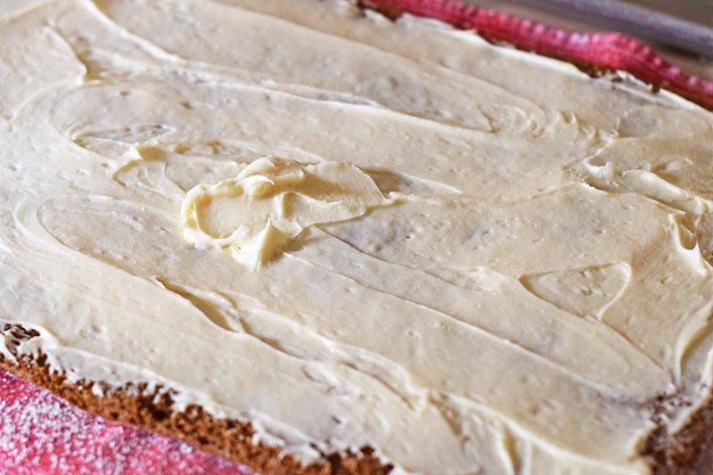 spread cream cheese filling onto pumpkin roll cake before rolling