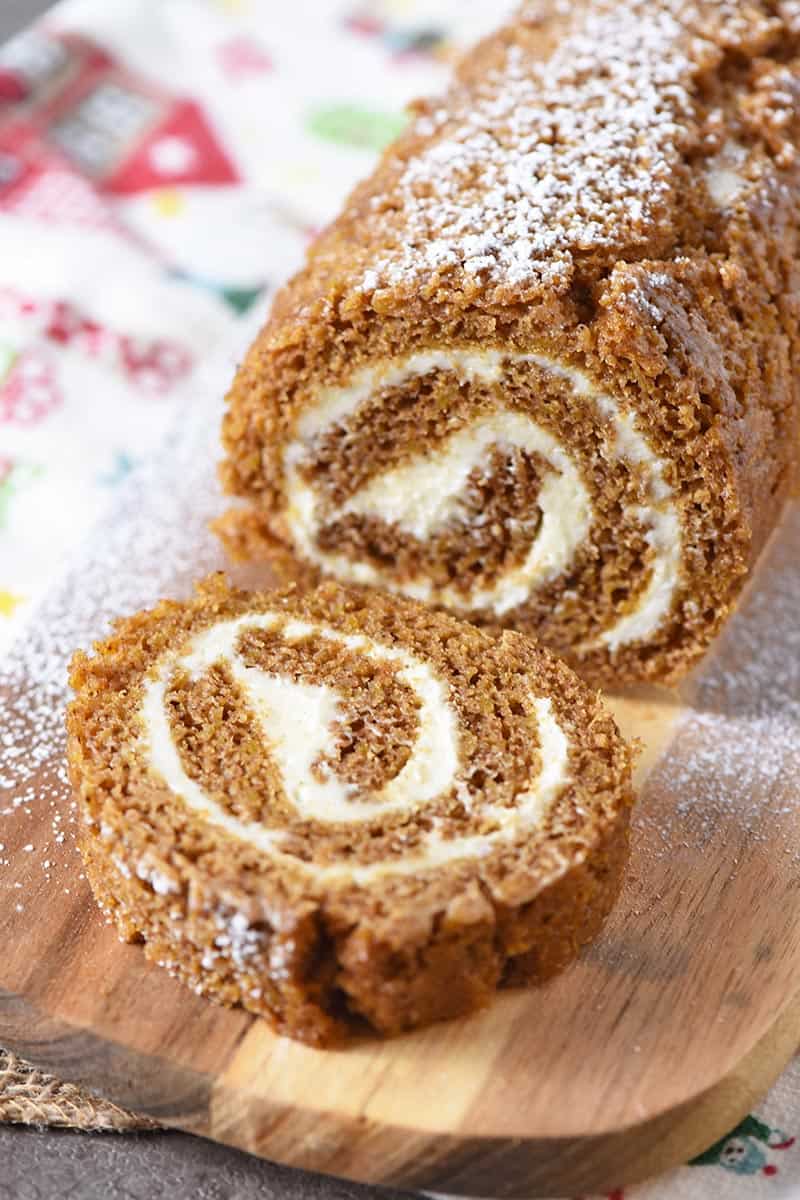 sliced pumpkin roll on a wooden cutting board with a holiday kitchen towel