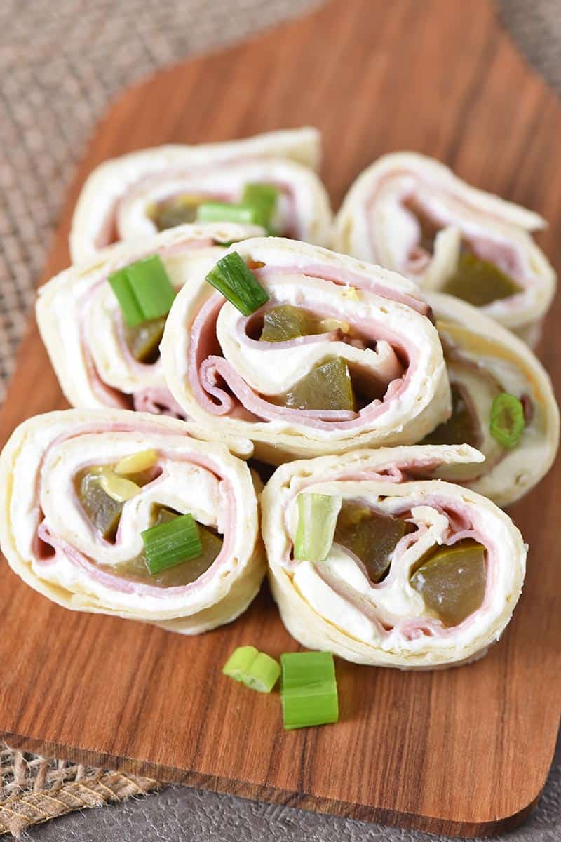 ham and dill pickle cream cheese pinwheels with chopped green onions on a small wooden cutting board