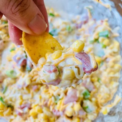 fingers holding corn chip with fiesta corn dip over bowl
