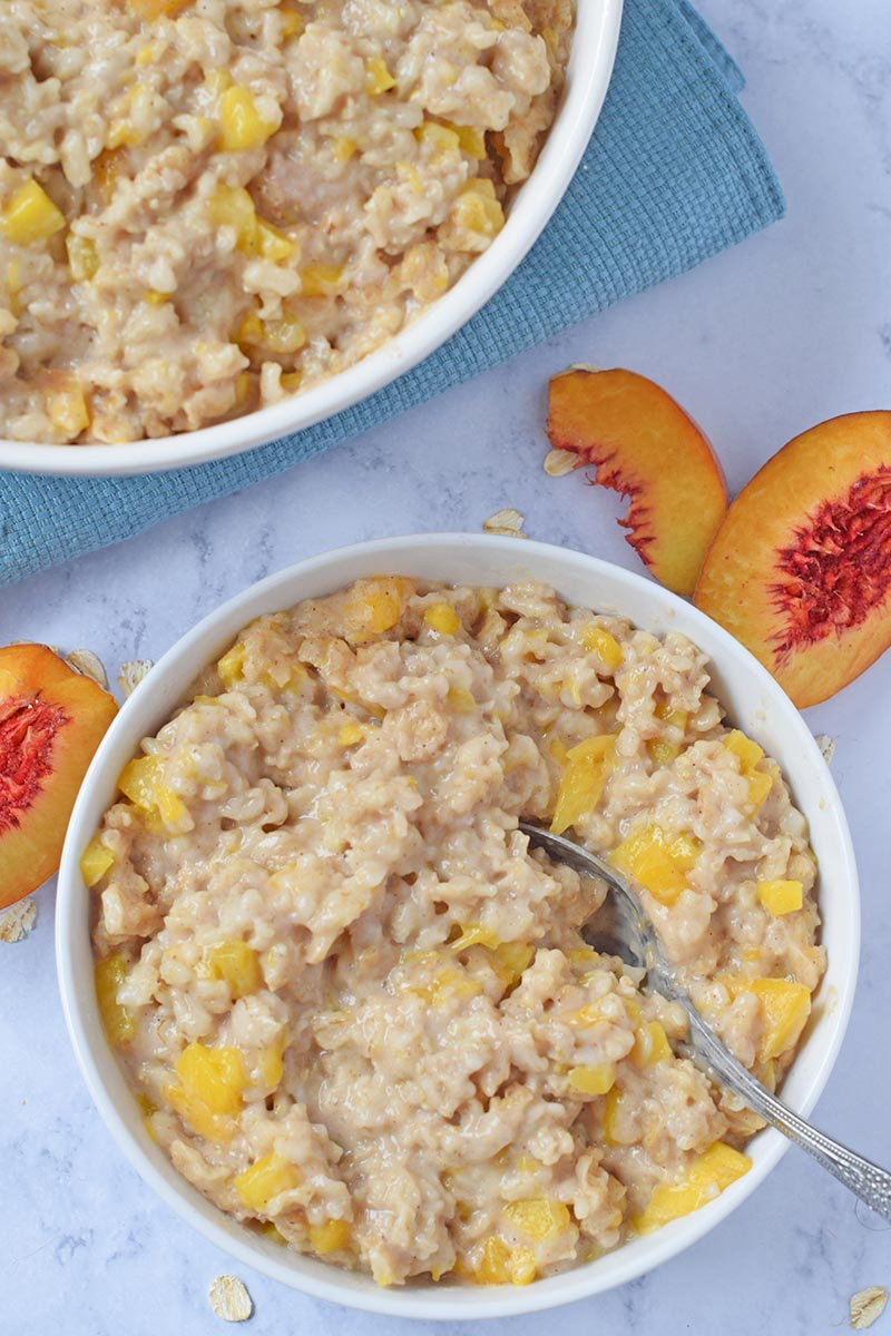 bowl of peach oatmeal made in the Instant Pot, on a white marble countertop with fresh peaches