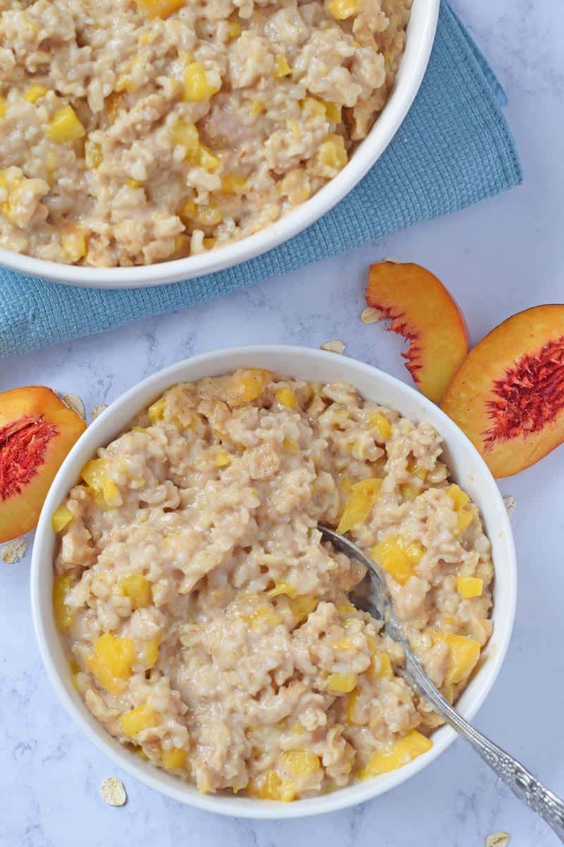 bowl of peaches and cream Instant Pot oatmeal on white marble countertop with blue placemat and fresh peaches