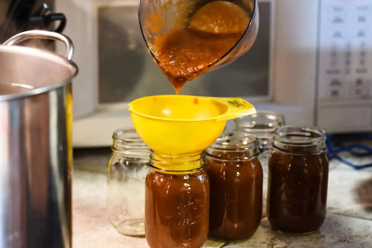 pouring apple butter in canning jars using a yellow jar funnel