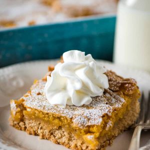 slice of pumpkin gooey butter cake topped with whipped cream on white plate with fork