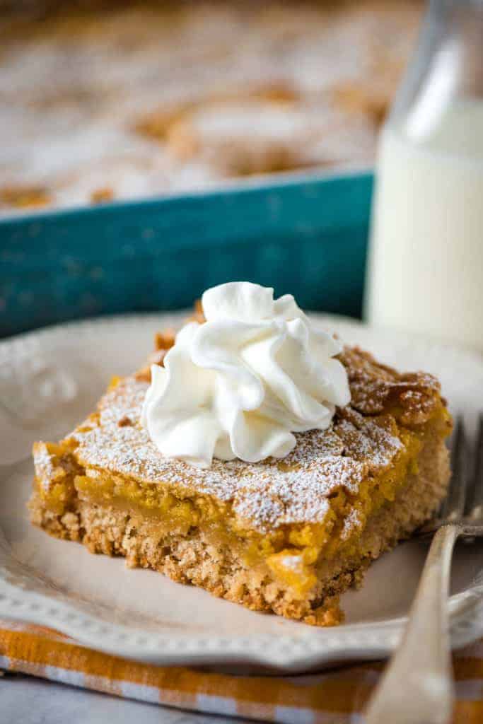 slice of pumpkin gooey butter cake topped with whipped cream on white plate with fork