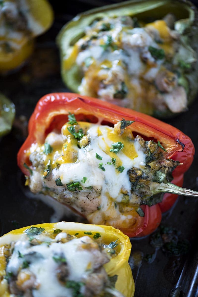 cooked chicken stuffed bell peppers on baking sheet with melted cheese and parsley