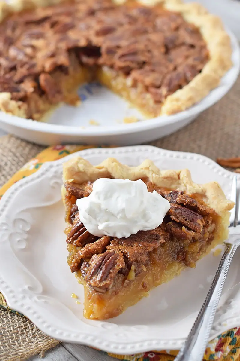 slice of classic pecan pie with whipped cream on white plate with fork