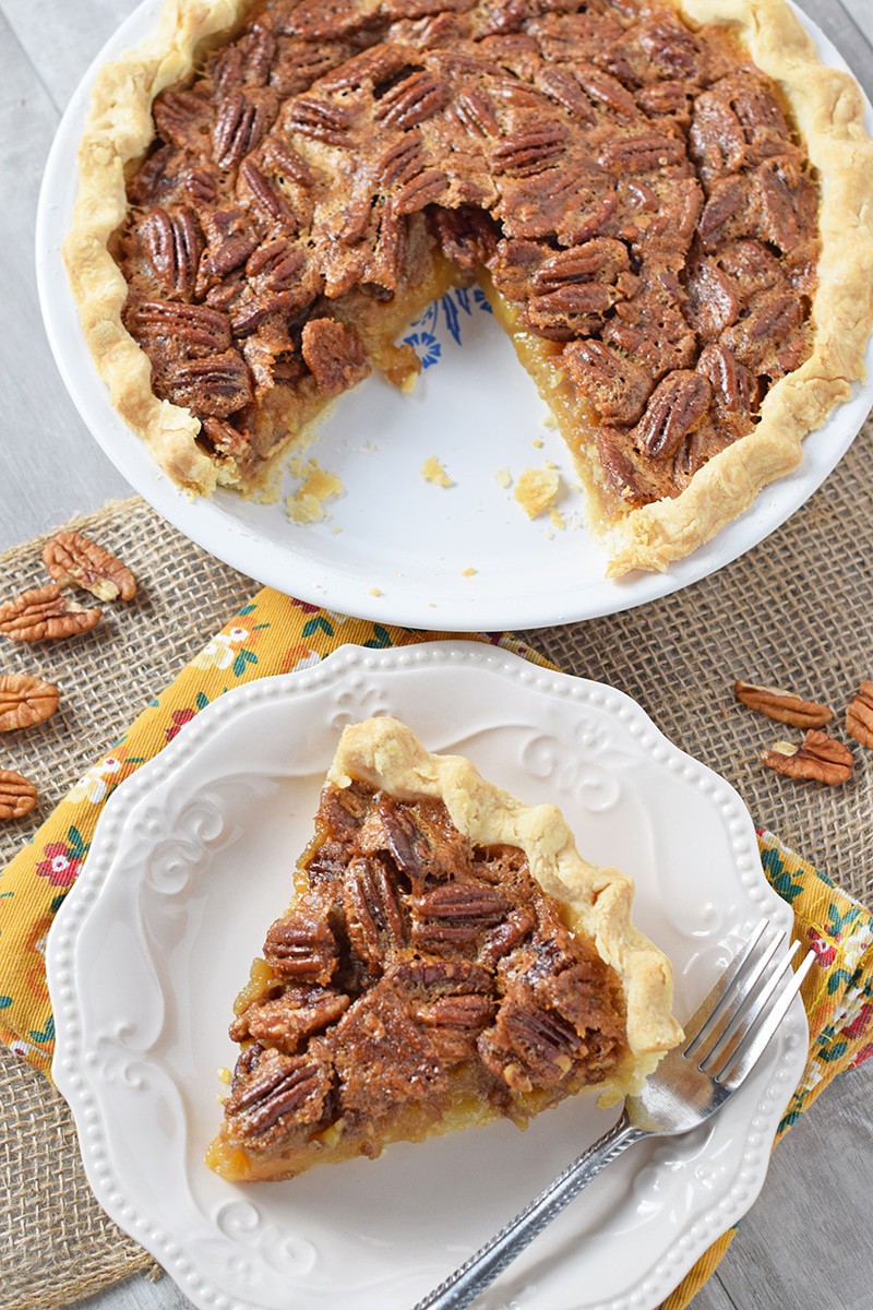 Whole pecan pie in Corningware pie plate with slice of pie on white plate with fork