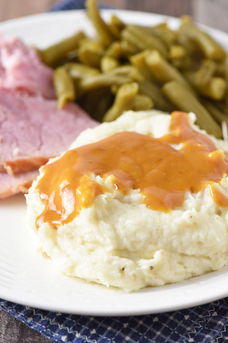 ham gravy on mashed potatoes served with ham and green beans on white plate