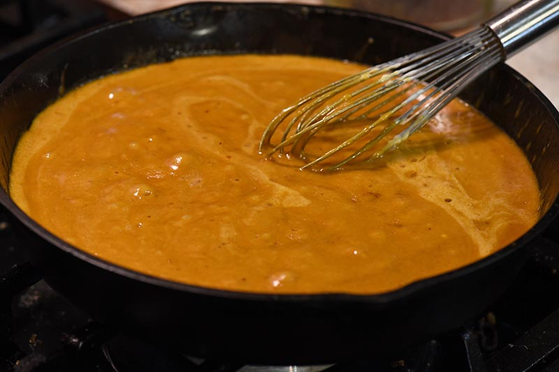simmering ham gravy recipe with drippings and whisking it until it thickens in cast iron skillet