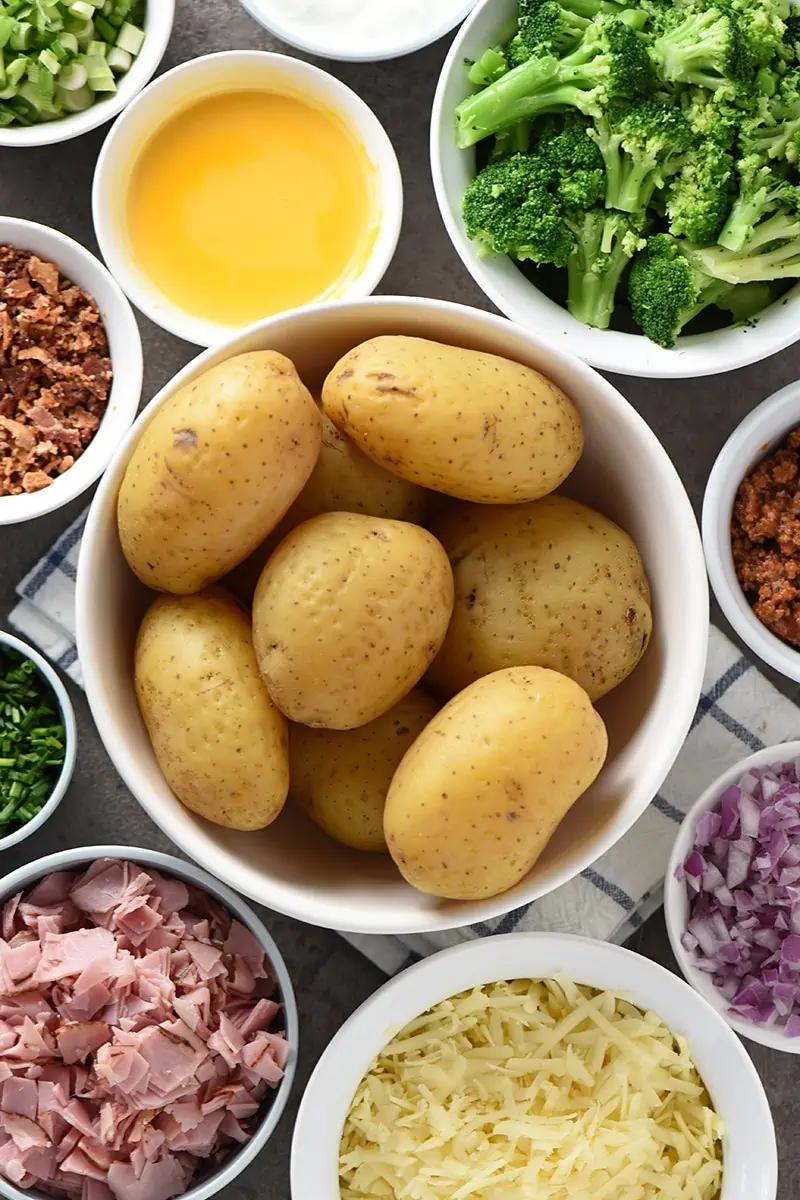 baked potato bar with baked potatoes in large white bowl and toppings in small bowls all around the potatoes