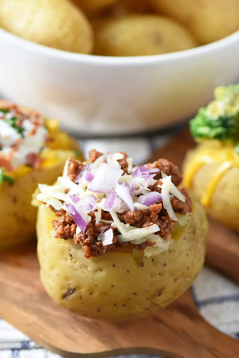 ultimate baked potato bar toppings, including sloppy joe ground beef, red onion, and shredded cheese, on wood cutting board