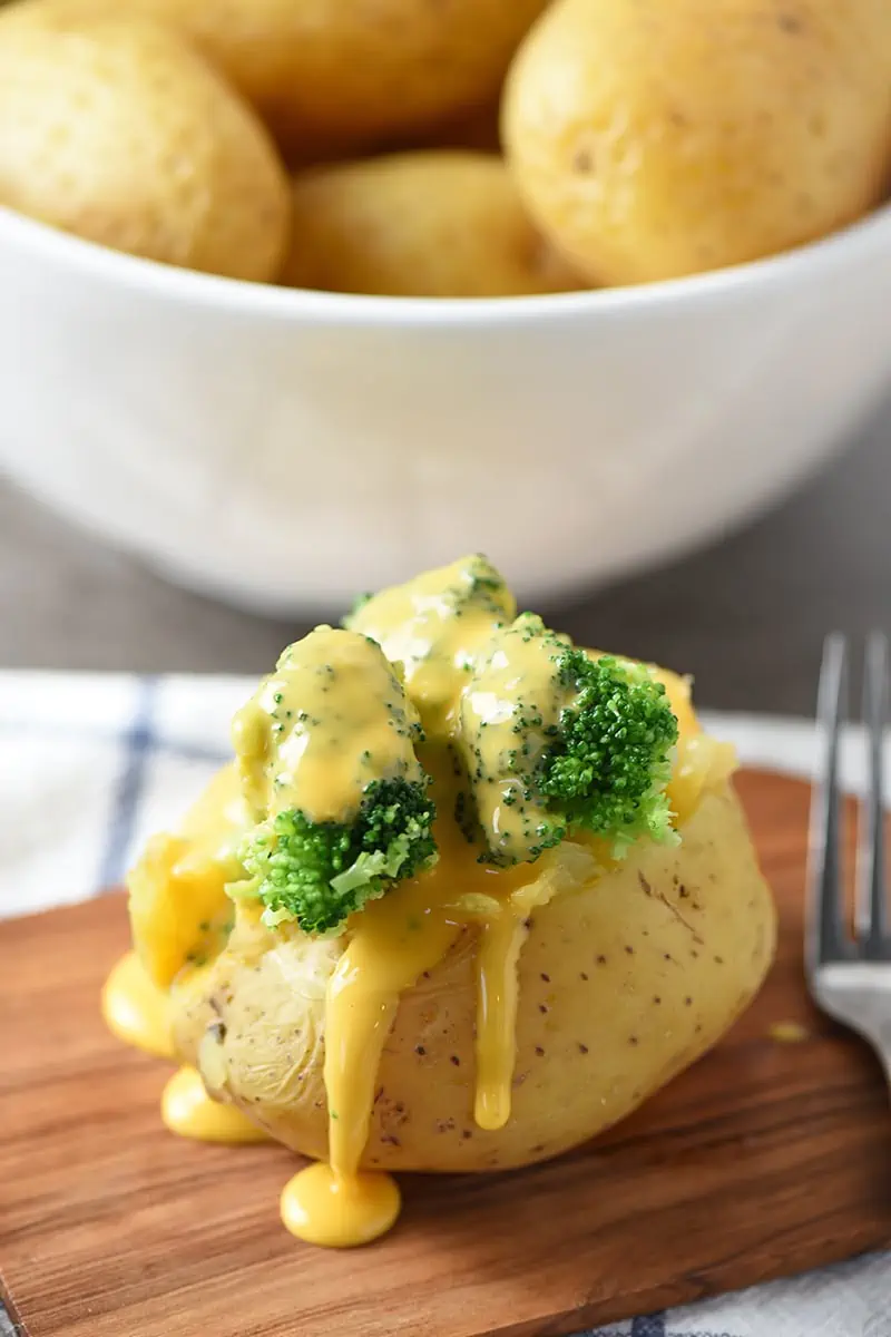 baked potato stuffed with broccoli and cheese sauce on wood cutting board