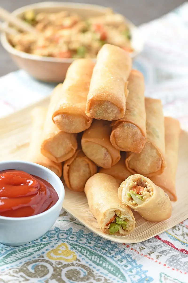 stacked fried rice spring rolls on bamboo plate with dipping sauce in small blue bowl