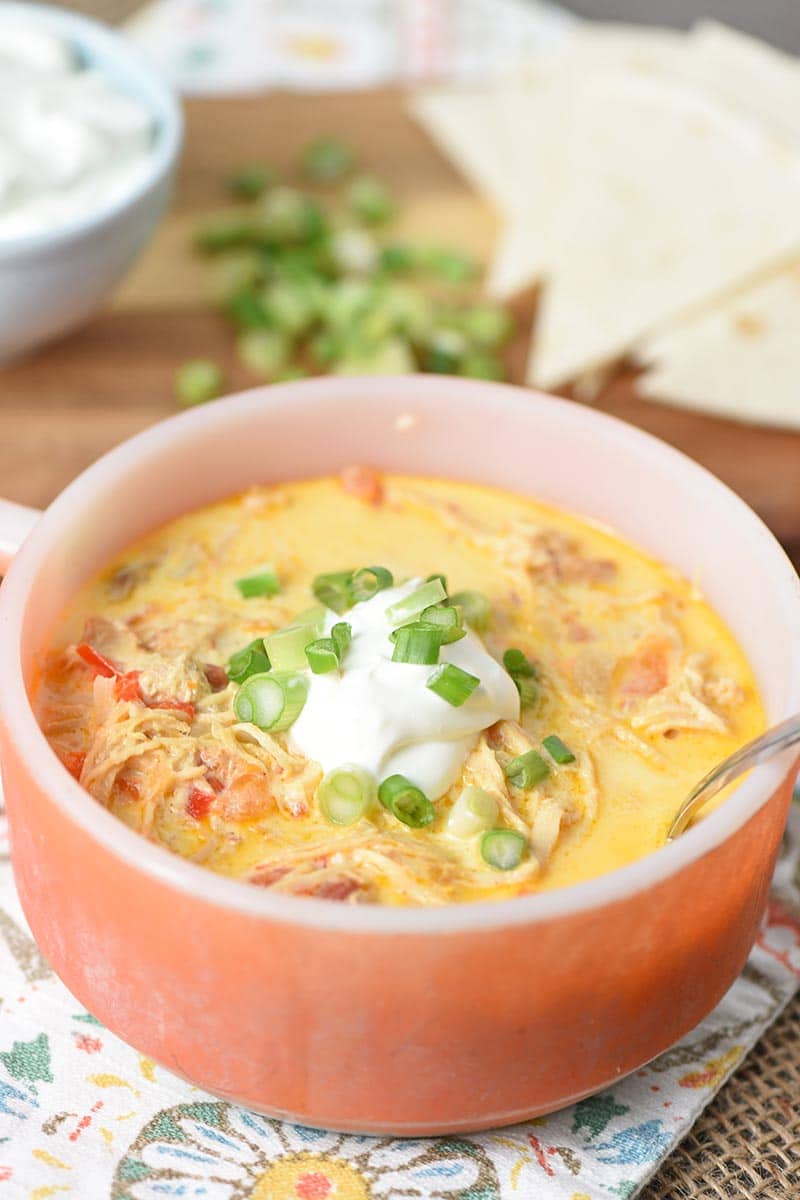 orange soup bowl with slow cooker chicken enchilada soup, a dollop of sour cream, and chopped green onions
