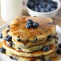 Blueberry Buttermilk Pancakes with maple syrup and fresh blueberries on a plate and milk to drink