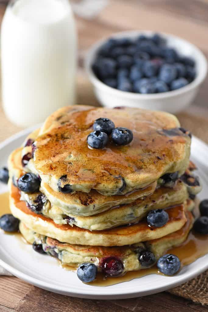 Blueberry Buttermilk Pancakes with maple syrup and fresh blueberries on a plate and milk to drink