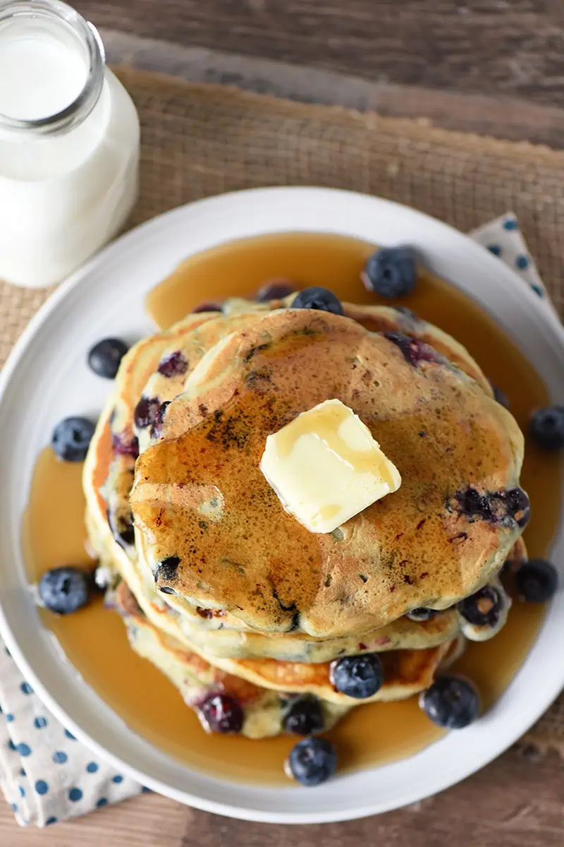 Blueberry Buttermilk Pancakes with butter and maple syrup on a plate, milk in a glass bottle on the side